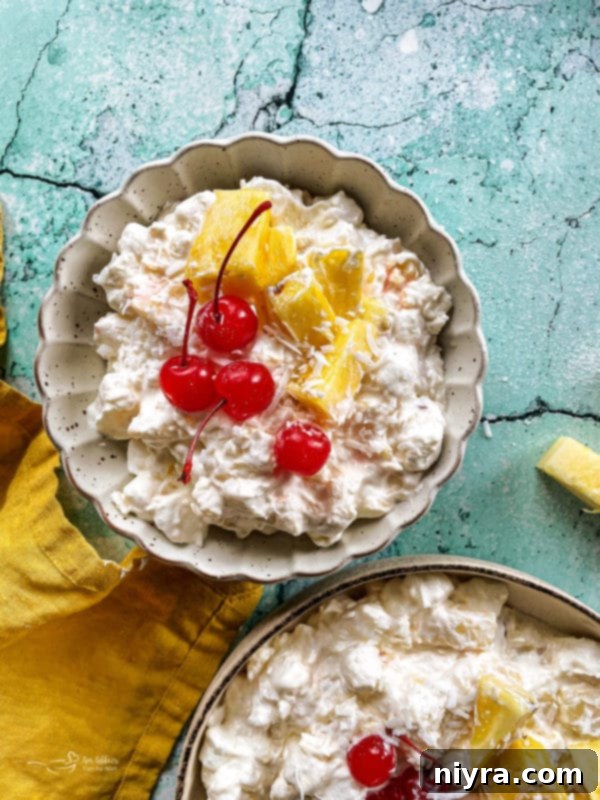 Two bowls of pineapple fluff dessert salad with cherries and diced pineapple, ready to be served.