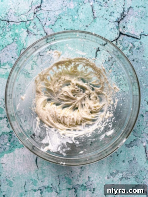 Top view of cream cheese, sugar, and coconut extract being beaten together in a bowl until fluffy.