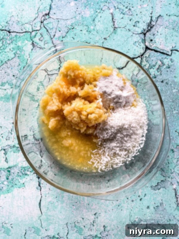 Crushed pineapple, instant coconut cream pudding mix, and flaked coconut combined in a clear bowl.