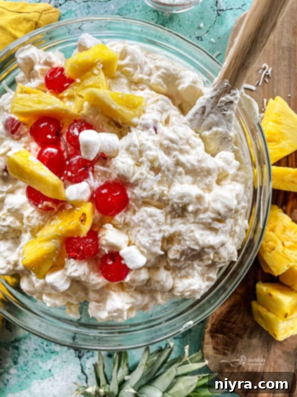 A bowl of piña colada fluff dessert salad with cherries and sliced pineapple, ready for chilling.