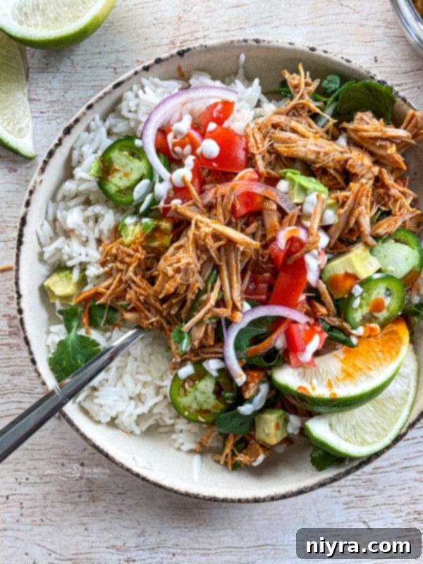 A vibrant bowl of Slow Cooker Cilantro Lime Pork served with fresh limes, juicy tomatoes, red onions, fluffy rice, and spicy jalapeños, showcasing its delicious appeal.