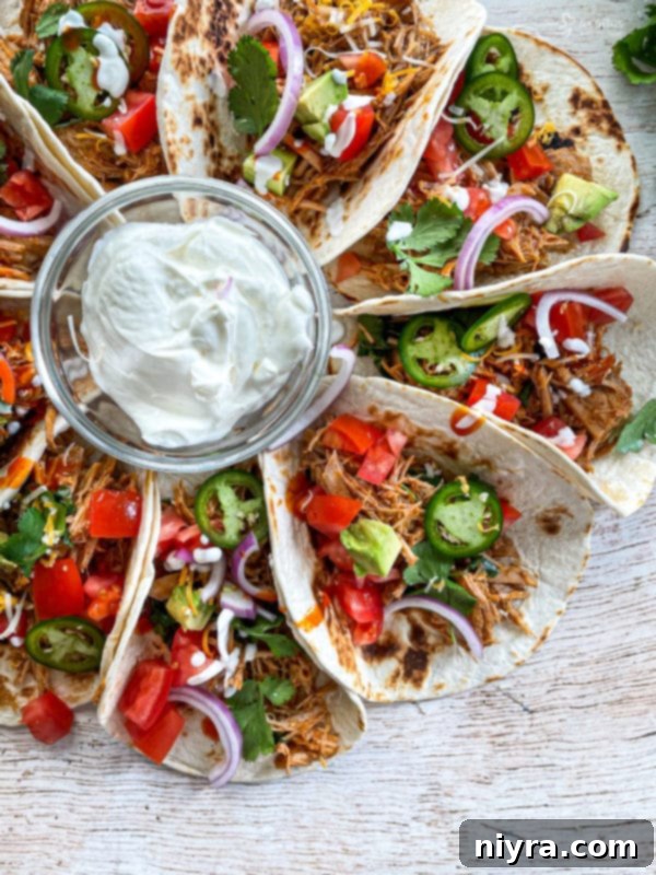 Top-down view of three soft tacos generously filled with slow cooker cilantro lime pork, garnished and ready to be served.