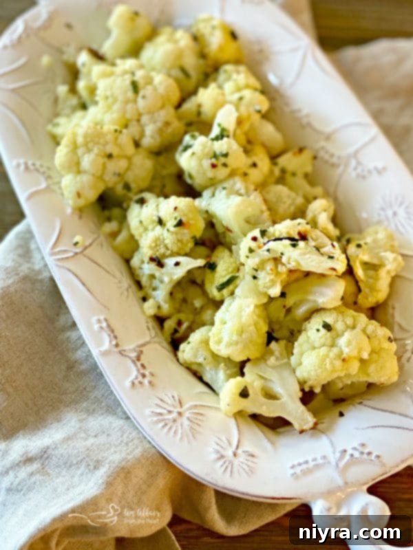 Crispy Roasted Cauliflower 2 Close-up of golden brown oven roasted cauliflower florets seasoned with garlic, red pepper, and thyme in a white dish, ready to serve.