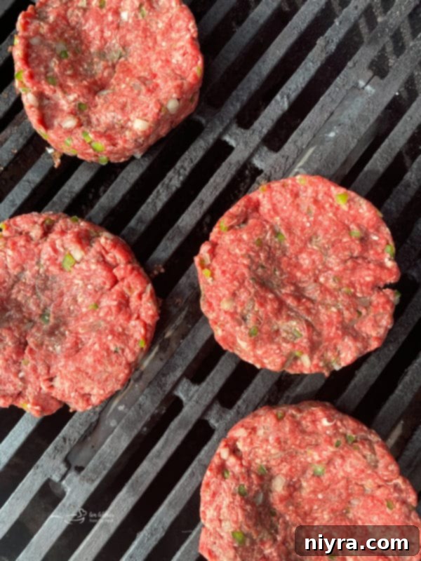 Hamburger patties cooking on an outdoor grill, with flames visible