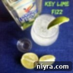 Overhead of key lime fizz, lime wedges, a shot glass and a bottle of Parrot Bay with text "Key LIme Fizz"