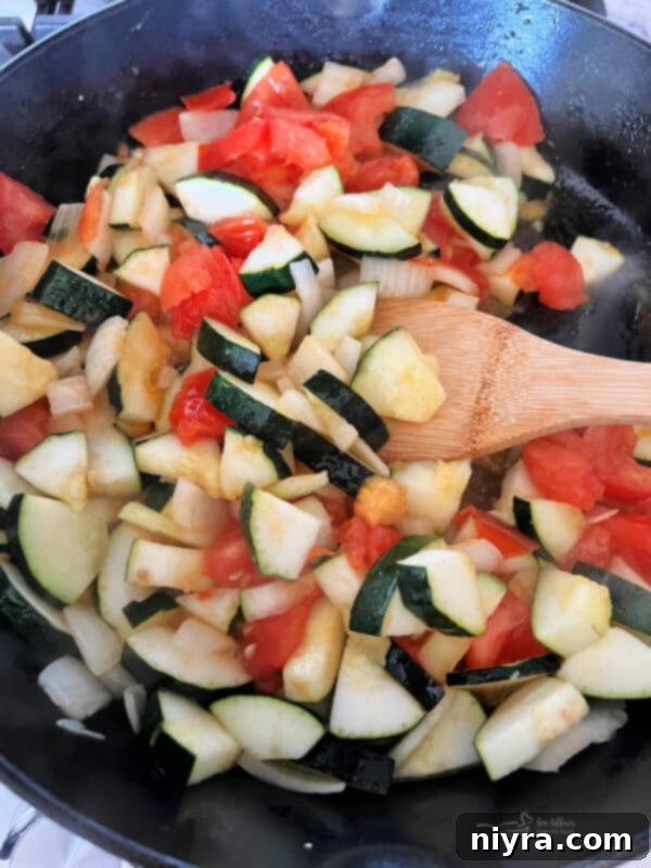 Zucchini, onions, and tomatoes sauteing in a skillet