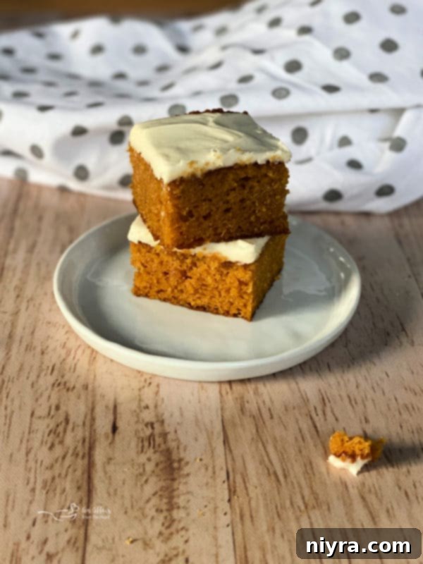 two carrot cake bars on white plate with cream cheese frosting