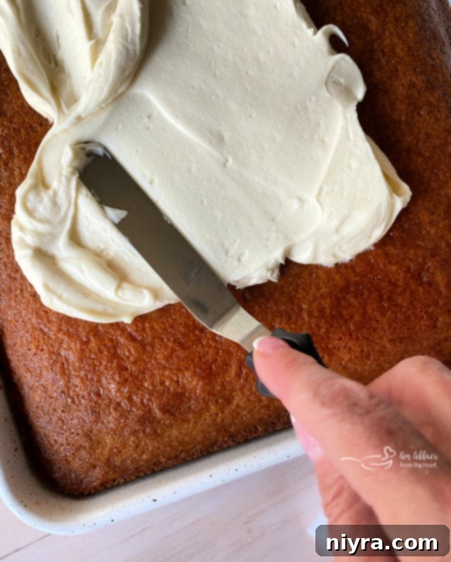 spreading cream cheese frosting on cooled carrot cake with baking tool