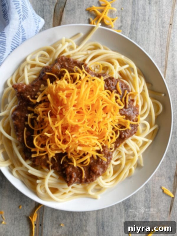 chili on a bed of noodles in a bowl, garnished with cheese