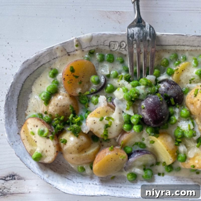 A fork taking a spoonful of creamed new potatoes and peas from a dish.
