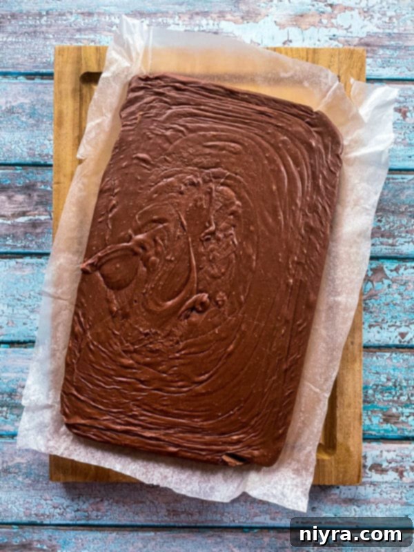 Smooth, melted chocolate orange fudge mixture spread evenly in a parchment-lined baking pan, ready for chilling and setting.