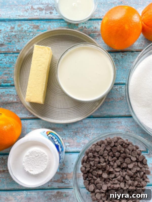 A collection of key ingredients for making Chocolate Orange Fudge: butter, cream, chocolate chips, marshmallow fluff, and fresh oranges, ready for preparation.