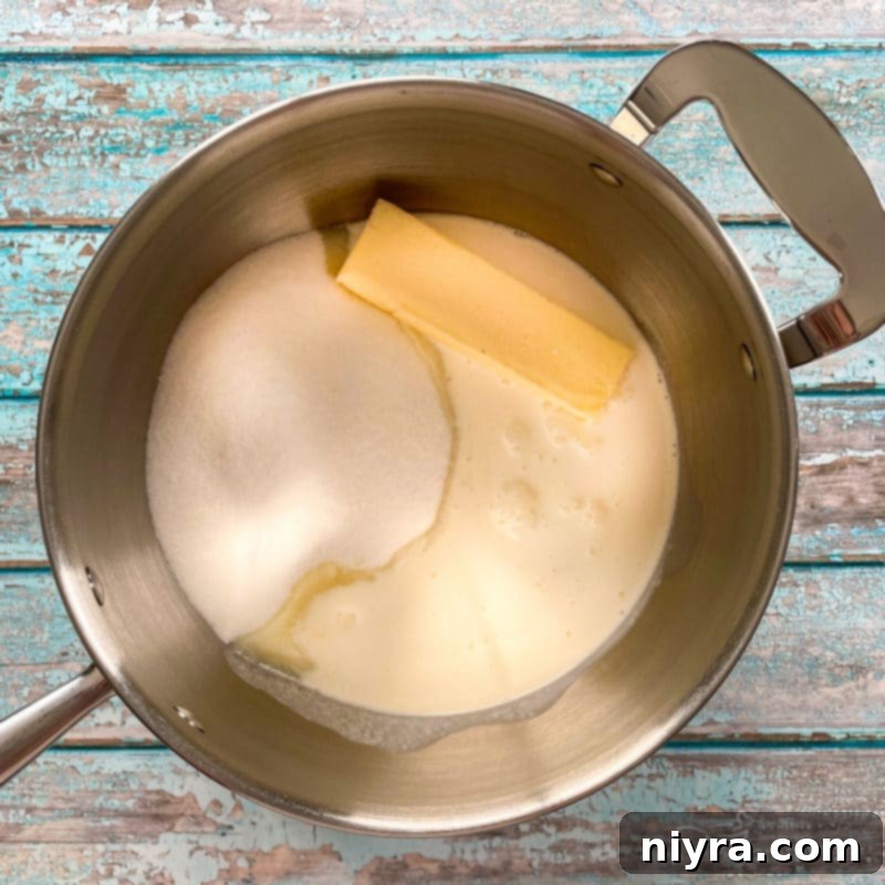 Melted butter, sugar, milk, and cream simmering in a saucepan, showing the beginning stage of cooking the fudge base to perfection.