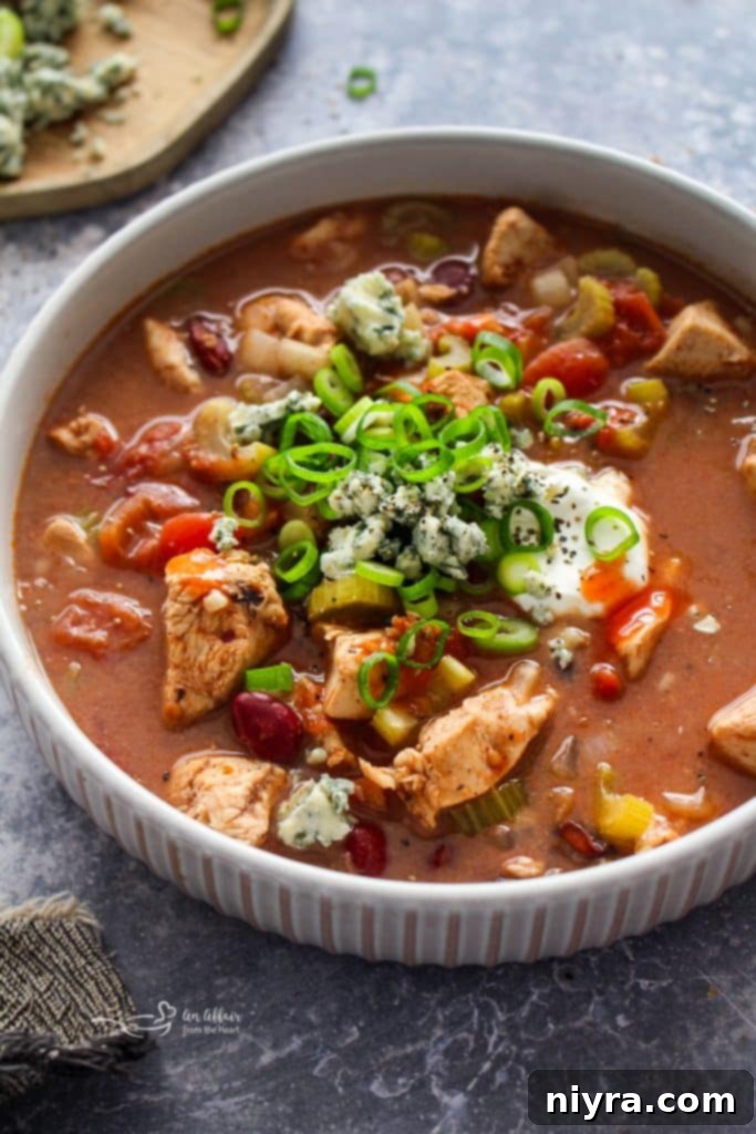 A bowl of Slow Cooker Buffalo Chicken Chili topped with ranch dressing and green onions.