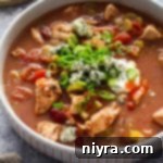 Close up of a bowl of Slow Cooker Buffalo Chicken chili topped with blue cheese, green onions, sour cream and hot sauce.