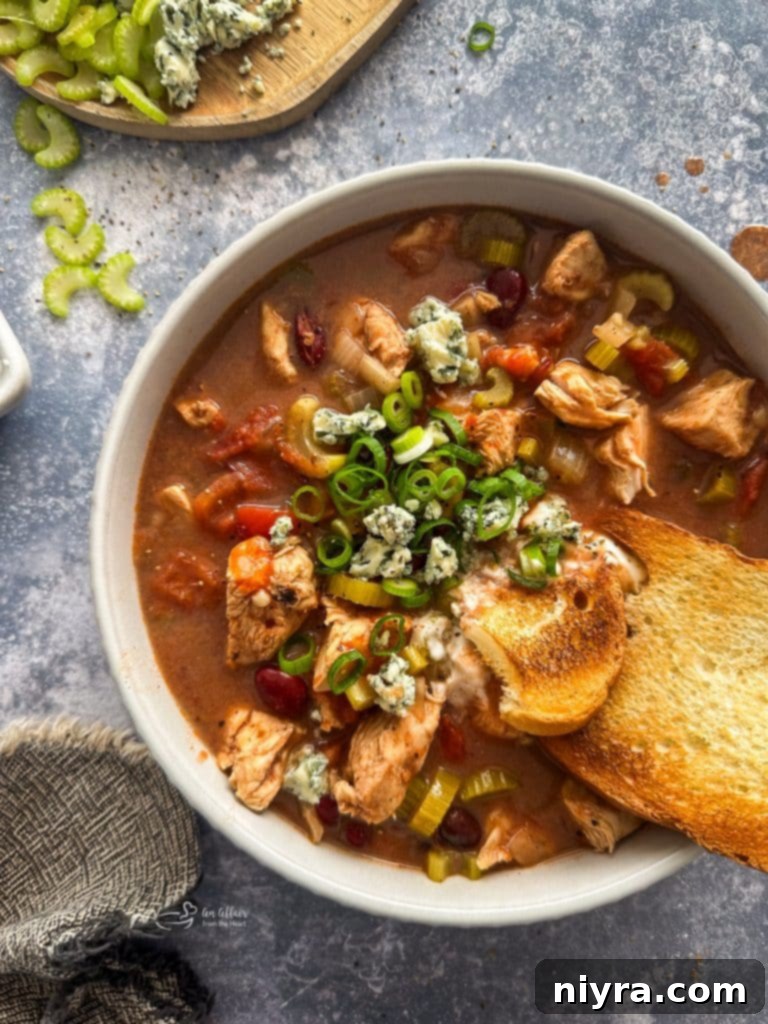 A beautifully presented bowl of Slow Cooker Buffalo Chicken Chili with various toppings, including blue cheese and green onions.