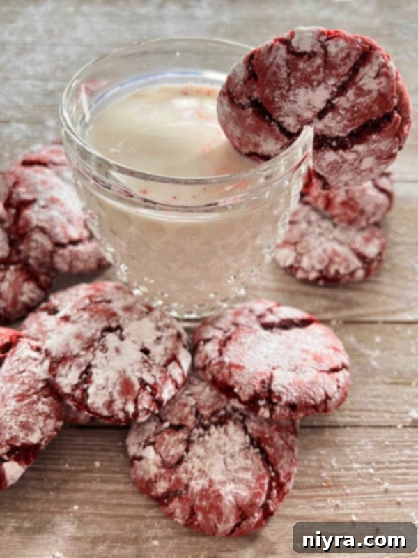 A festive red velvet crinkle cookie, perfectly powdered, being dipped into a tall glass of fresh milk, capturing a moment of sweet enjoyment.