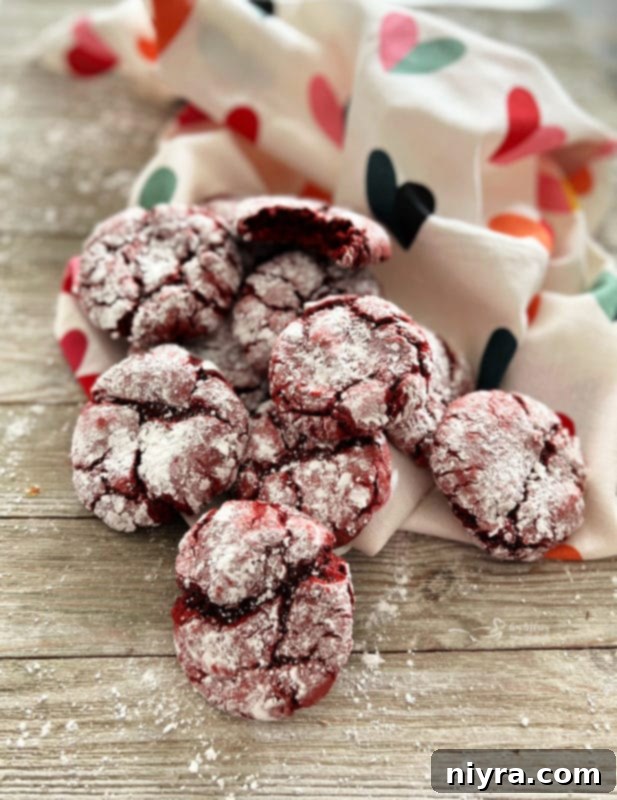 Close-up view of red velvet crinkle cookies, generously coated in powdered sugar, showcasing their signature crackled surface, ready to be enjoyed.