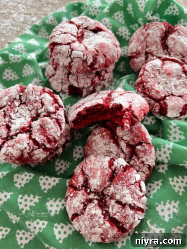 A stack of freshly baked red velvet crinkle cookies resting on a green fabric, highlighting their soft texture and snowy powdered sugar coating.