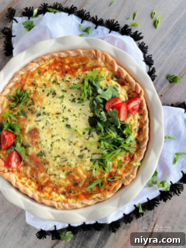 An overhead view of a Green Chile Quiche with Sausage, garnished with fresh cilantro and tomato slices.