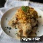 Golden Baked Stuffed Pork Chops 3 Baked pork chop on a plate with stuffing and herbs on top with mushroom gravy