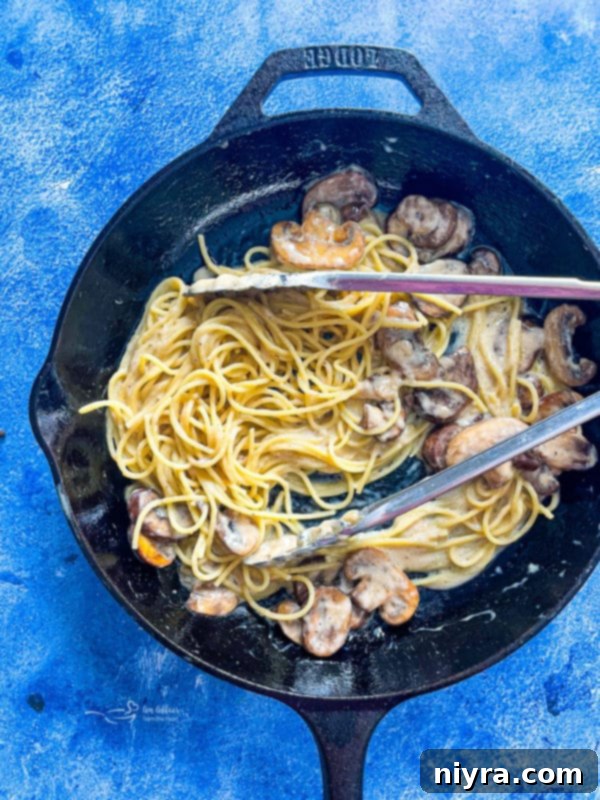 Cooked spaghetti noodles tossed with sautéed mushrooms in a skillet, coated in a creamy sauce, ready to be served.
