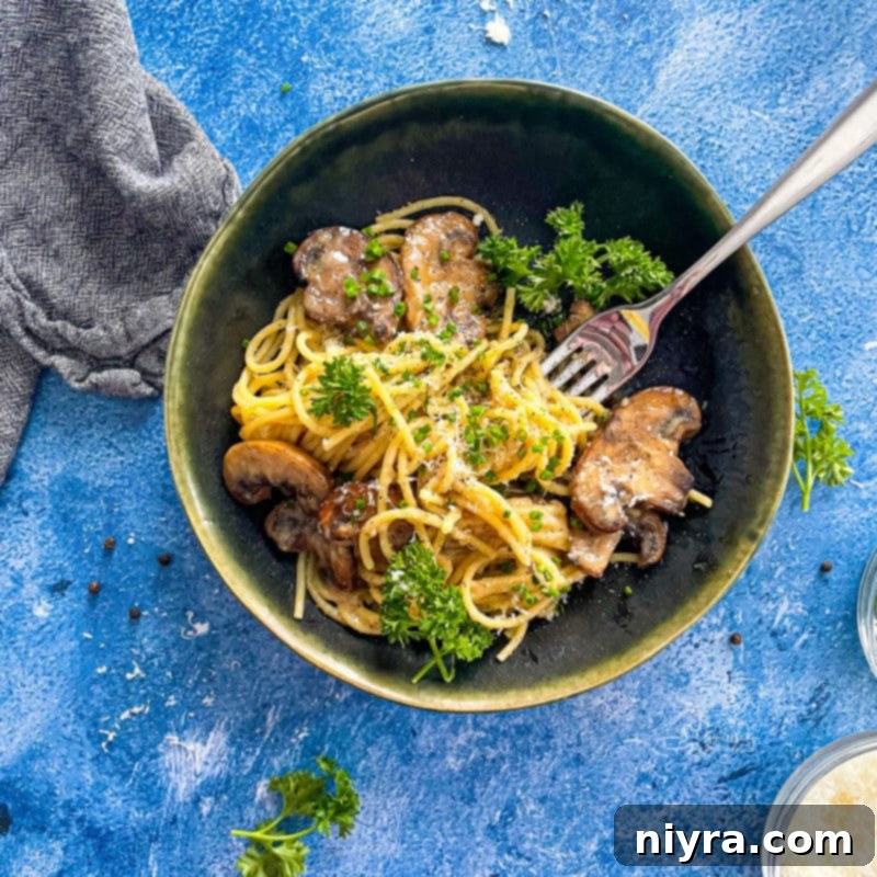 A close-up of a bowl of Cacio e Pepe with mushrooms, a fork, and scattered fresh herbs, highlighting the creamy sauce and tender pasta.