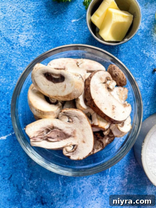 A close-up of a bowl filled with sliced raw mushrooms, glistening with melted butter, ready to be cooked for a dish.