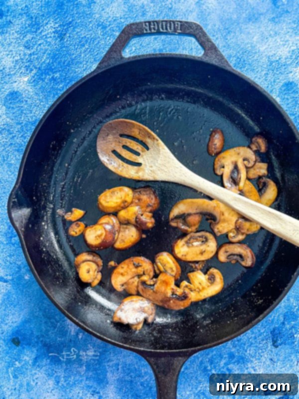 Sliced mushrooms cooking in a hot skillet with olive oil and butter, beginning to brown and soften.