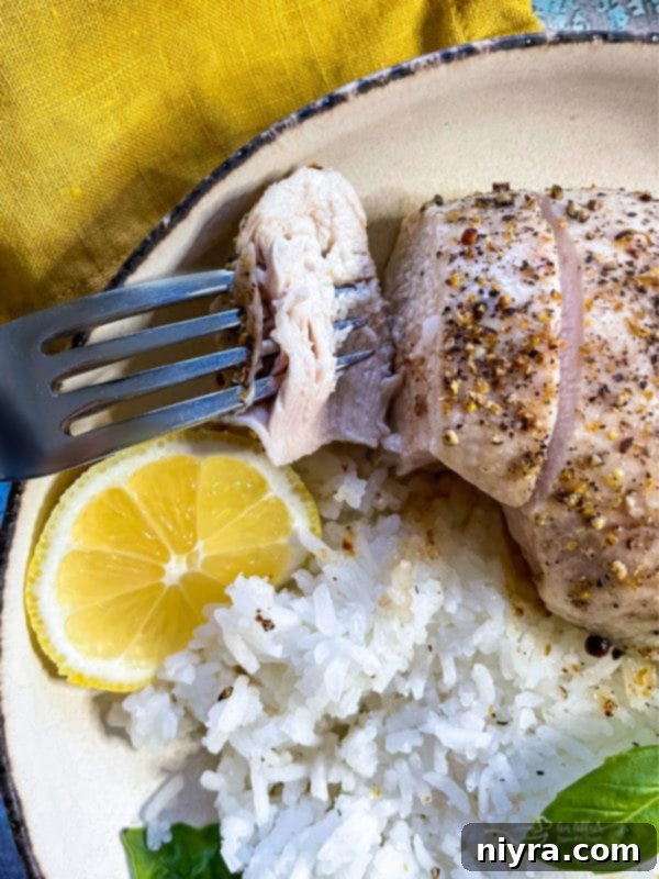 A plate of lemon pepper chicken with a fork, lemon wedge, rice, and fresh basil.