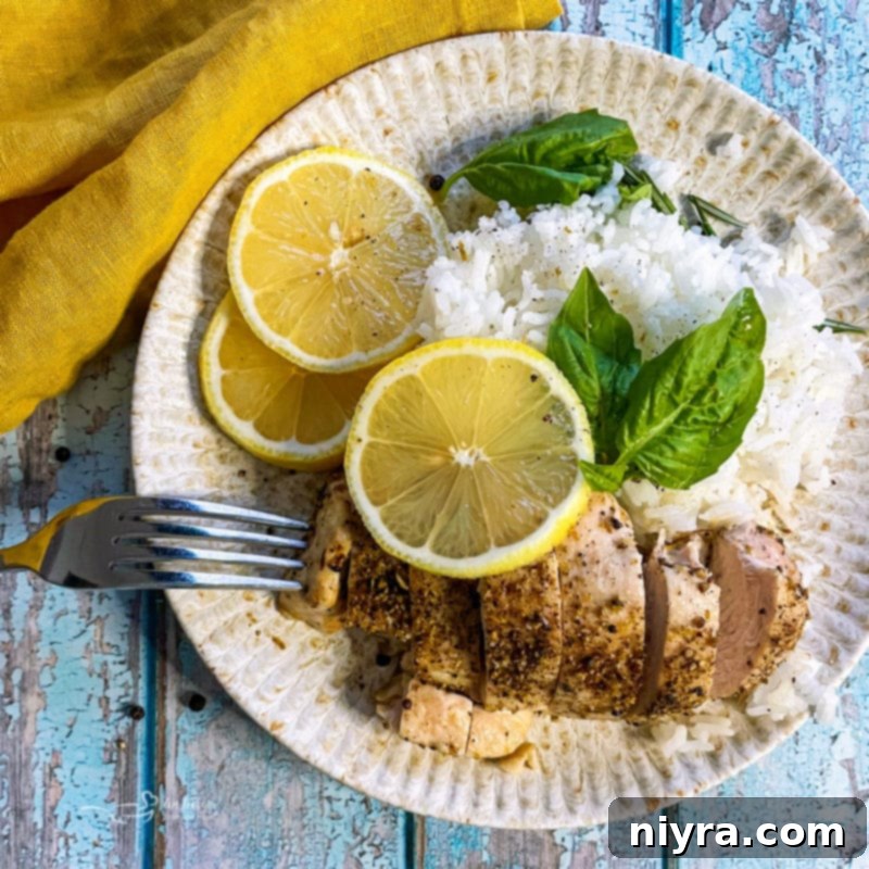 Overhead shot of lemon pepper chicken with rice, lemon slices, and herbs on a white plate.
