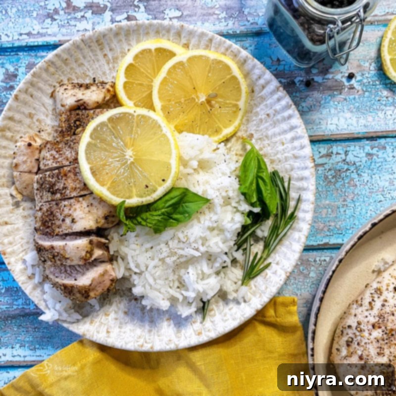 A beautifully plated lemon pepper chicken breast with rice, lemon slices, and basil garnish.
