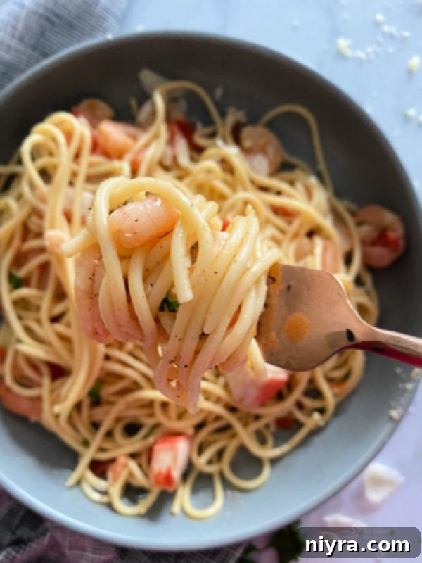 A close-up shot of a serving of Shrimp and Crab Pasta in a white bowl, showing the creamy sauce and fresh ingredients.