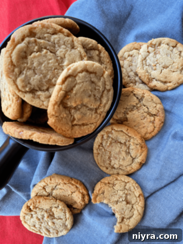 Overhead shot of warm Butter Brickle Cookies in a rustic bowl and scattered on a wooden table, invitingly delicious.