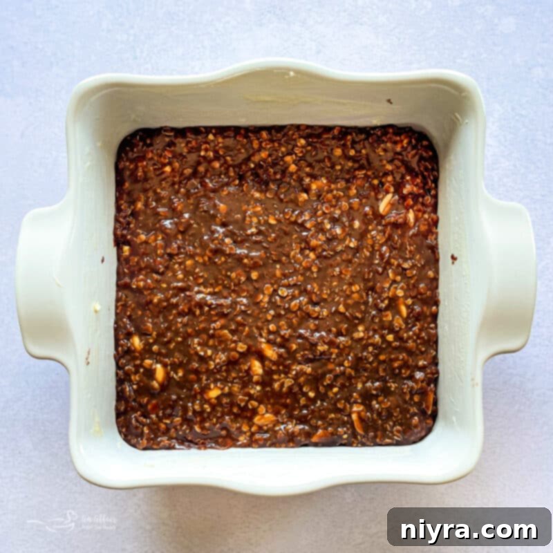 Peanut butter, vanilla, oatmeal, and peanuts being stirred into the hot chocolate mixture in a saucepan.