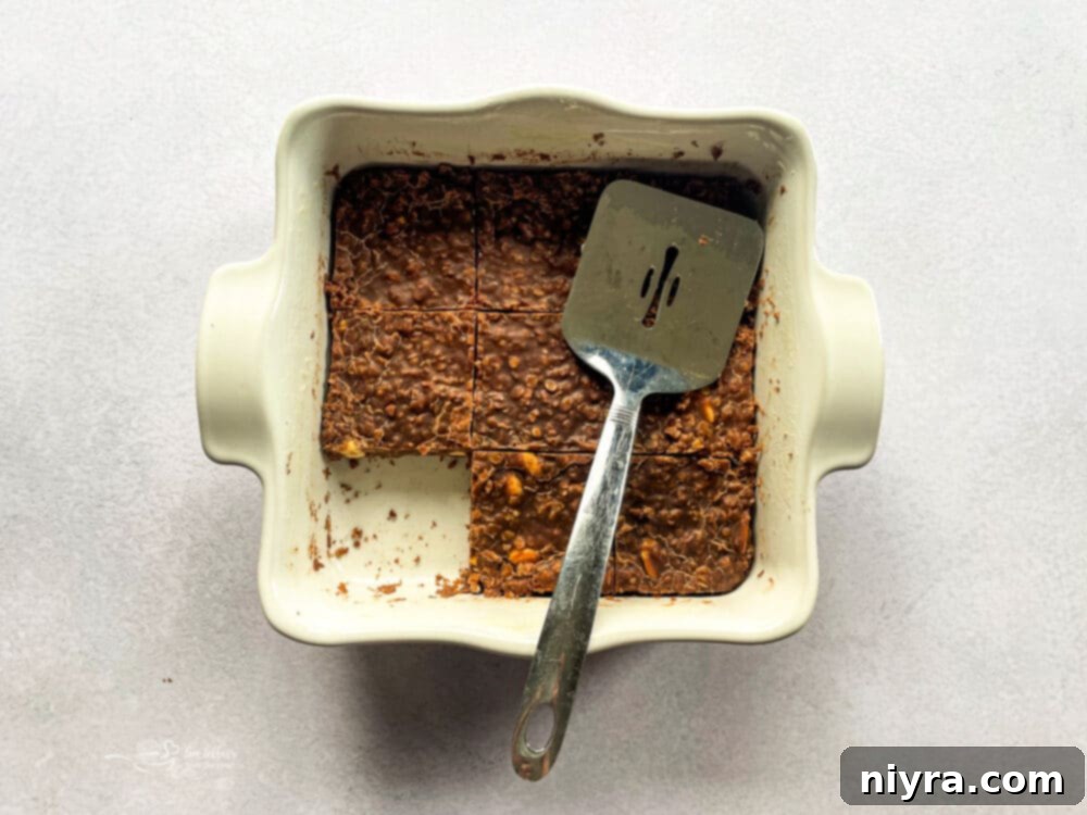 No-bake chocolate peanut butter mixture being pressed firmly into a parchment-lined baking dish.