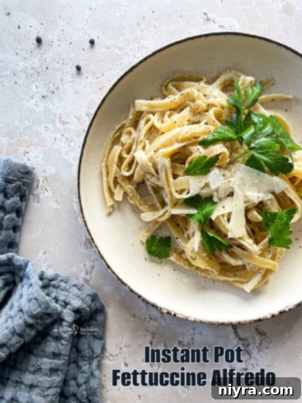 A beautiful top-down shot of a large serving dish filled with Instant Pot Fettuccine Alfredo, garnished with fresh parsley.