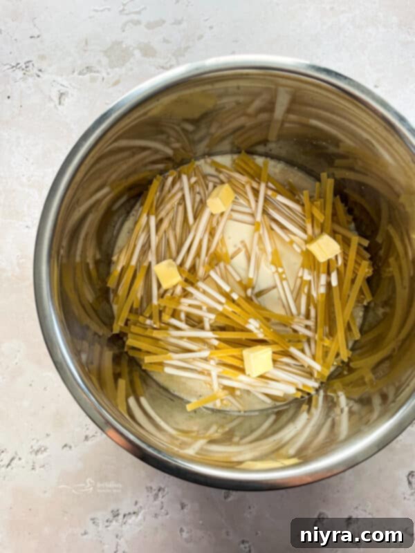 Fettuccine noodles layered crisscross in the Instant Pot, topped with heavy cream and butter.