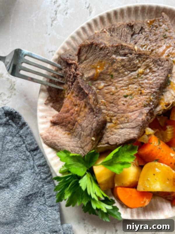 Close-up of a perfectly cooked, sliced Bob Evans style pot roast on a plate, surrounded by tender carrots, potatoes, and parsnips, with a rich gravy.
