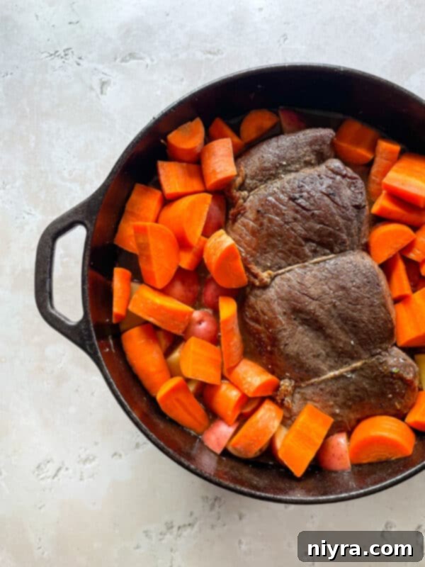 The Dutch oven, with its contents of roast and vegetables simmering in broth, being carefully placed into the preheated oven.