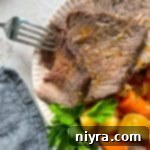 close up of copycat Bob Evans pot roast sliced with a fork in one piece on a cream colored scalloped plate.