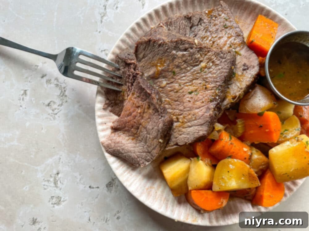 Large cut of braised pot roast with a side of mixed vegetables including potatoes, carrots, and parsnips, all drizzled with a rich brown gravy on a white platter.