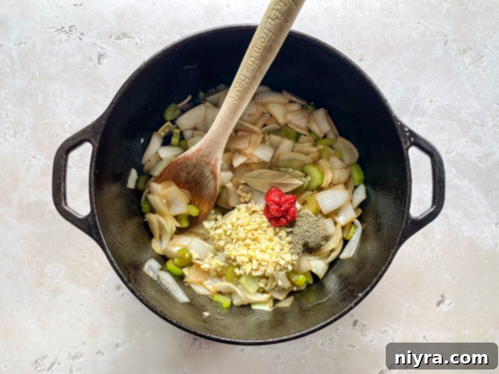 Tomato paste, minced garlic, thyme, and bay leaves added to the softened onions and celery in a Dutch oven, releasing their aromatic flavors.