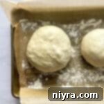 Rolled pizza dough balls on a parchment-lined baking sheet, ready for final proofing.