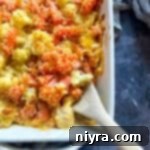 Cauliflower and Carrot Gratin and a wooden serving spoon in a white baking dish close up.