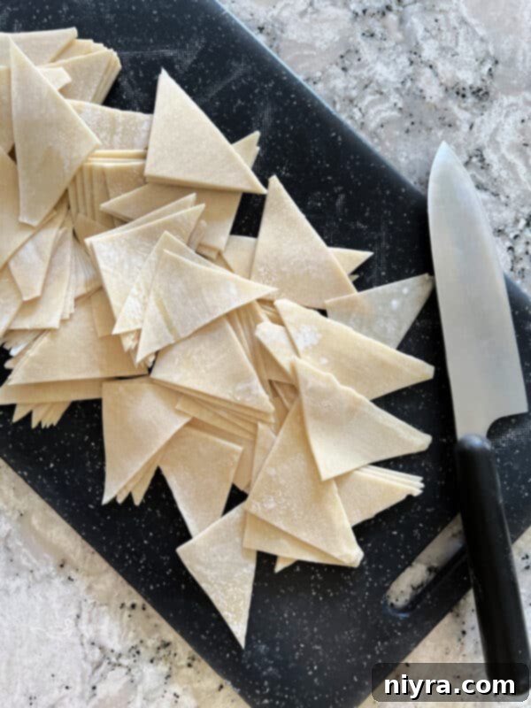 Air fryer wonton wrappers being cut into quarters on a cutting board, ready for cooking.