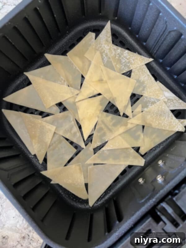 Wonton wrappers carefully placed in a single layer in an air fryer basket, ready for cooking.
