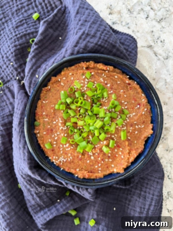 A close-up of a bowl of Asian Bean Dip, showcasing its creamy texture and the vibrant green onions and toasted sesame seeds used as garnish, next to a variety of fresh vegetables for dipping.