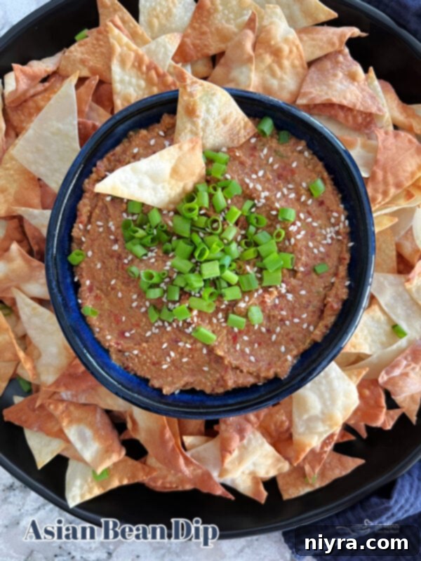 A beautifully presented bowl of Asian Bean Dip, garnished with fresh herbs and sesame seeds, placed prominently on a clean white background, highlighting its vibrant appearance.