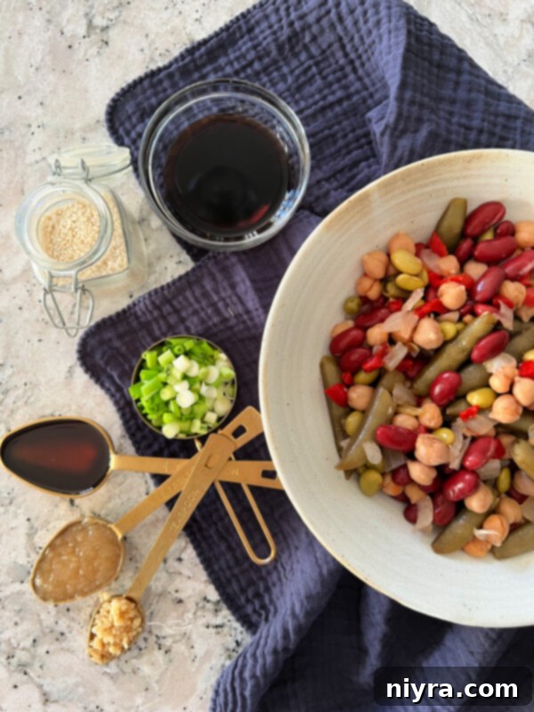 A bowl of Asian Bean Dip, garnished with green onions and sesame seeds, sits prominently on a dark surface, ready for dipping.